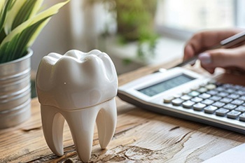 Large model tooth next to hand calculating cost with calculator